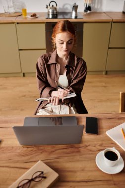 Sakin bir mutfakta, kızıl saçlı bir kadın yaratıcılığını keşfetmek için notlar ve fikirler çizer..