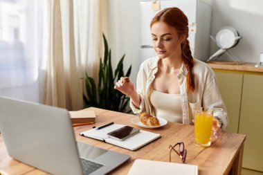 Güzel kızıl saçlı bir kadın laptopuyla çalışırken kahvaltıya daldı..