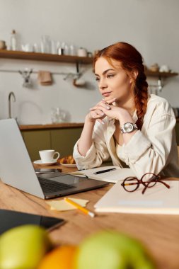 Kızıl saçlı bir kadın özenle dizüstü bilgisayarı üzerinde çalışıyor sıcak bir evde..