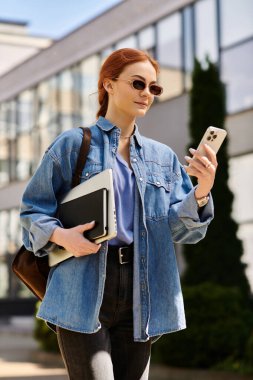 Parlak giyimli, kızıl saçlı bir kadın şehir manzarasında yürüyor, telefonuna bir amaç için bakıyor..