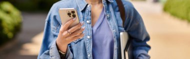 Kızıl saçlı kadın akıllı telefonunu kullanarak güneşli bir yolda güvenle yürüyor..