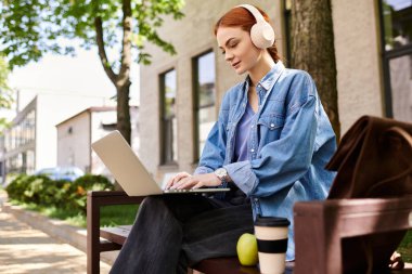 Laptopuyla meşgul olan kızıl saçlı bir kadın ağaçların altında sıcak bir günün tadını çıkarıyor..