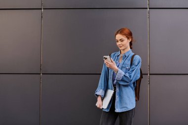 Kot ceketli, rahat, kızıl saçlı bir kadın dışarıda sakin bir gülümsemeyle telefonunu kontrol ediyor..