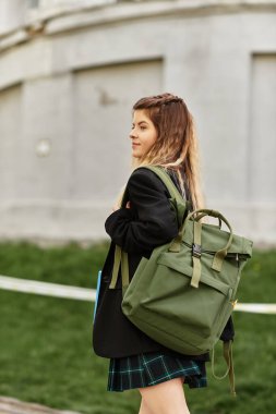 Şık üniformalı genç bir kadın canlı bir üniversite kampüsünde güven içinde geziniyor..