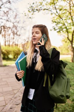 Güzel bir üniversiteli kız sıcak bir öğleden sonra elinde kitaplarla telefonuyla sohbet ediyor..