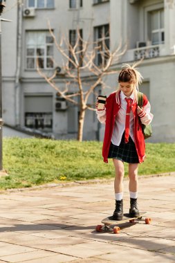 Şık bir üniversiteli kız elinde kahve fincanıyla güneşli bir günde kaykayına biniyor..