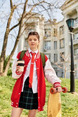 Şık bir üniversiteli kız, elinde kaykayıyla kahvesini yudumluyor ve gençlik enerjisi saçıyor..