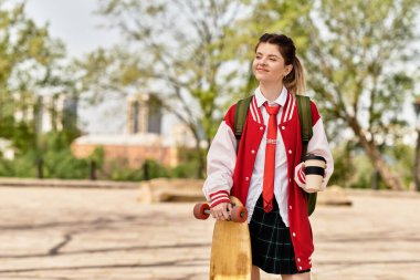 Genç bir üniversite öğrencisi elinde kaykayla kampüste güzel bir gün geçiriyor..