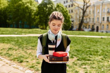 Şık giyinmiş genç bir öğrenci güneşli bir günde kitap ve kahve taşıyor..