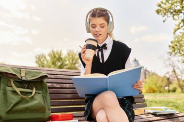 Üniversiteli kız bir bankta oturur, kahvesini yudumlar ve şık kıyafetiyle kitap okur..