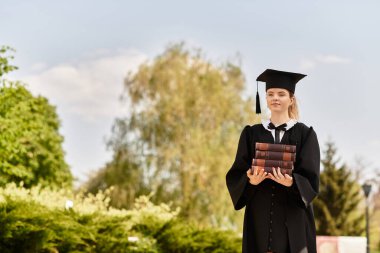 Gururlu bir mezuniyet elbisesi içinde kitap tutuyor ve başarısını dışarıda kutluyor..