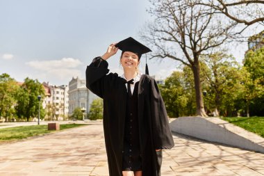 Mezuniyet elbisesi içinde gülümseyen genç bir kadın dışarıda başarısını kutluyor..