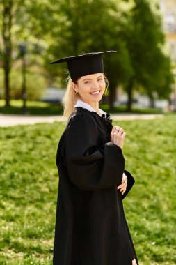 Genç bir üniversiteli kız parkta mezuniyet elbisesi ve şapkasıyla gururla gülümsüyor..