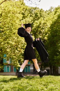 Neşeli bir üniversiteli kız mezuniyet elbisesi ve şapkasıyla başarısını kutluyor..