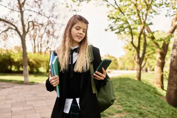 Genç üniversite öğrencisi açık havada güneşli bir günün tadını çıkarıyor. Denge kitapları ve akıllı bir telefon..