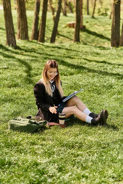 Genç yetişkinler yemyeşil çimlerde oturur, sakin bir parkta yanında defterlerle ders çalışmaya odaklanırlar..