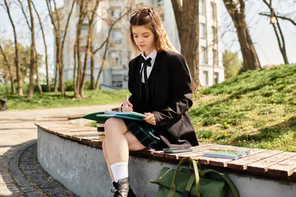 Güzel bir üniversite öğrencisi bankta oturur, çalışır ve sakin bir kampüs parkında notlar alır..