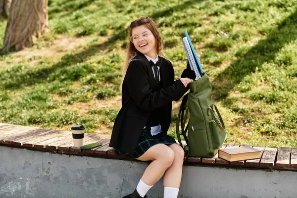 Neşeli bir öğrenci üniversitede sırt çantasını açarken sırtüstü oturur ve gülümser..