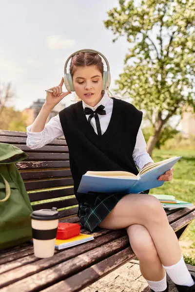 Genç bir üniversiteli kız bankta oturur, derslerine odaklanır, parkta güneşli bir günün tadını çıkarır..