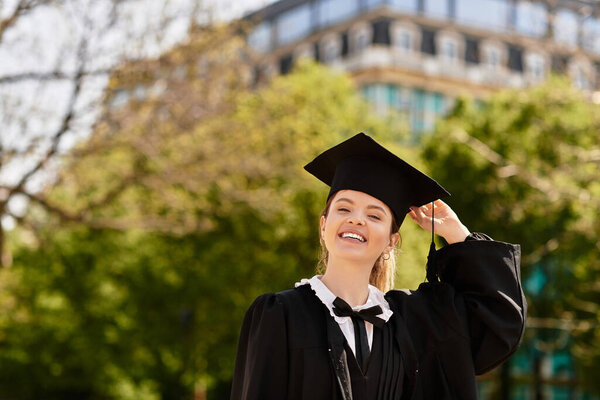 Молодая женщина излучает радость и достижения во время ношения выпускного платья и шапки в природе.