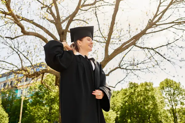 Neşeli bir üniversiteli kız mezuniyet elbisesi ve şapkasıyla gururla poz veriyor, bir dönüm noktasını kucaklıyor..