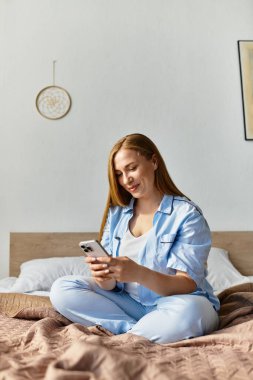 Genç bir kadın rahat bir şekilde yatağında oturuyor, rahat bir evde akıllı telefonuyla meşgul oluyor..