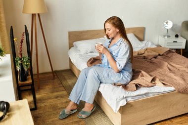 Genç bir kadın, yatak odasında sıcak bir içeceğin tadını çıkarırken rahat bir şekilde giyinir..