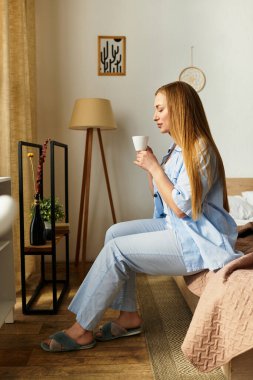 Güzel, genç bir kadın evinde rahat bir şekilde oturup rahatlarken sıcak içeceğinin tadını çıkarıyor..