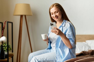 Genç bir kadın rahat bir şekilde evinde dinleniyor, telefonunu kullanırken gülümsüyor ve içkisini yudumluyor..