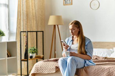 Genç bir kadın rahat evinde rahat bir şekilde yatağında otururken telefonuna sarılıyor..