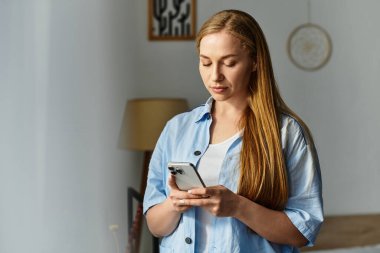 Güzel bir kadın evinde duruyor, rahat bir anı yakalıyor, akıllı telefonuna odaklanıyor..