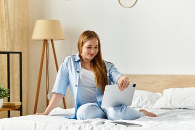 Genç ve güzel bir kadın, sıcak bir ev ortamında tabletiyle meşgul olarak yatağında dinleniyor..