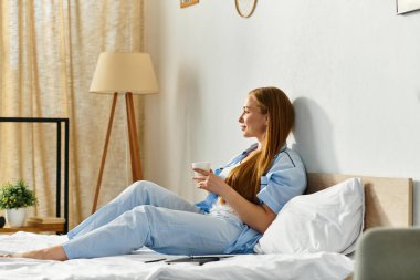 Genç bir kadın evinde rahatça rahatlar, sıcak ortamının tadını çıkarırken içkisini yudumlar..