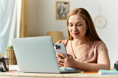 Kadın evde rahatlar, akıllı telefonunu düzenli bir masada otururken mutlu bir şekilde kullanır..