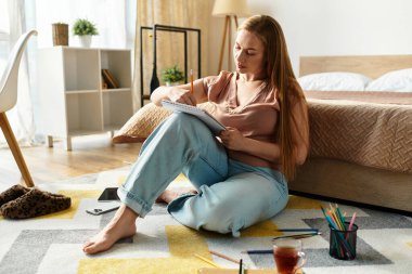 Genç bir kadın evinde yaratıcı bir andan zevk alıyor, düşünceli bir şekilde halının üzerinde çizim yapıyor..