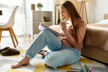 Genç bir kadın yerde oturuyor, defterine yazıyor, rahat bir havanın tadını çıkarıyor..