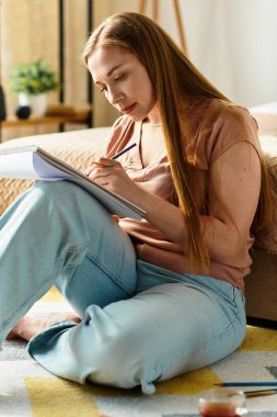 Genç bir kadın yerde oturuyor, defterine çizim yapıyor, evde yaratıcılıkta kayboluyor..