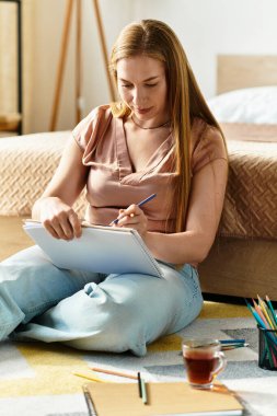 Genç bir kadın yerde oturuyor, ışıkla dolu huzurlu ve rahat bir odada çizim yapıyor..