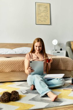 Sıcak, genç bir kadın tabletle yerde oturuyor, çayını yudumluyor ve ev atmosferinin tadını çıkarıyor..