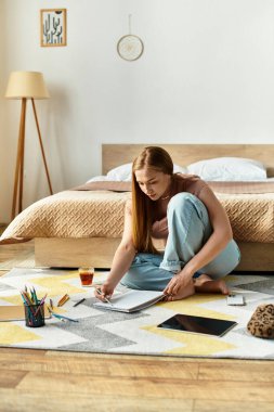 Genç bir kadın rahat yatak odasında yerde oturmuş, parlak kalemlerle çeşitli tasarımlar çiziyor..