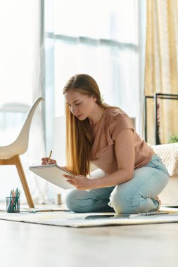 Genç bir kadın yerde diz çöküp, güneş ışığında çizim yaparak sıcak bir atmosfer yaratıyor..