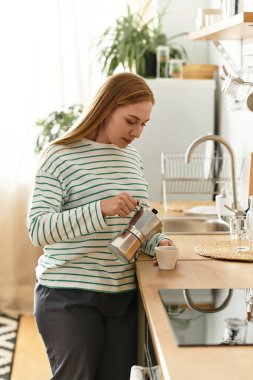 Kadın sıcak mutfağında duruyor, bir fincana kahve doldururken sükunetin tadını çıkarıyor..