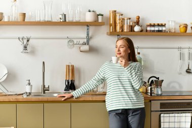 Genç bir kadın davetkar mutfağında sıcak bir fincan kahvenin keyfini çıkarıyor, evinde huzuru kucaklıyor..