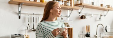 Sıcak bir mutfakta genç bir kadın sıcak içkisinin tadını çıkarırken ev ortamının tadını çıkarıyor..