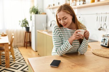 Genç bir kadın evinde dinleniyor, çay içiyor ve telefonuna sıcak bir şekilde bakıyor..