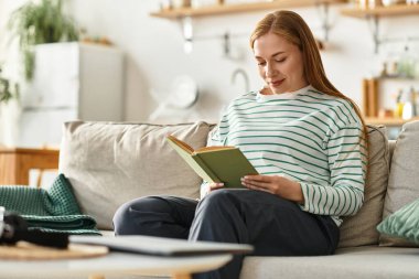 Genç bir kadın evinde rahat bir kanepede kitap okurken huzurlu bir anın tadını çıkarıyor..