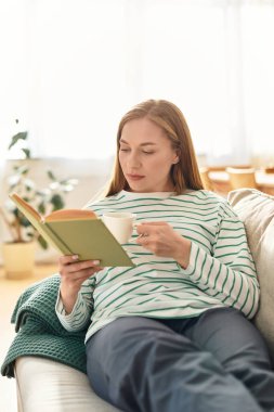 Genç bir kadın sıcak ve davetkar bir atmosferle çevrili çayı yudumlarken kitap okumaktan hoşlanır..
