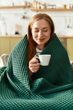 Genç bir kadın evine davet ederken battaniyeye sarılıp ılık bir içkinin tadını çıkarıyor..