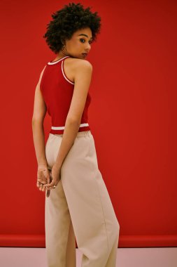 Şık genç kadın zarif poz veriyor, çarpıcı kırmızı duvara karşı şık kıyafetini vurguluyor..