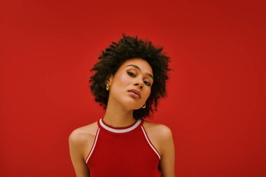 Genç bir kadın, özgün tarzını sergileyerek, koyu kırmızı bir zemine karşı özgüvenle poz verir..